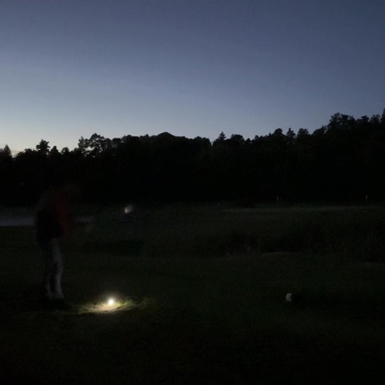 En person slår till en golfboll som börjar lysa upp på en golfbana