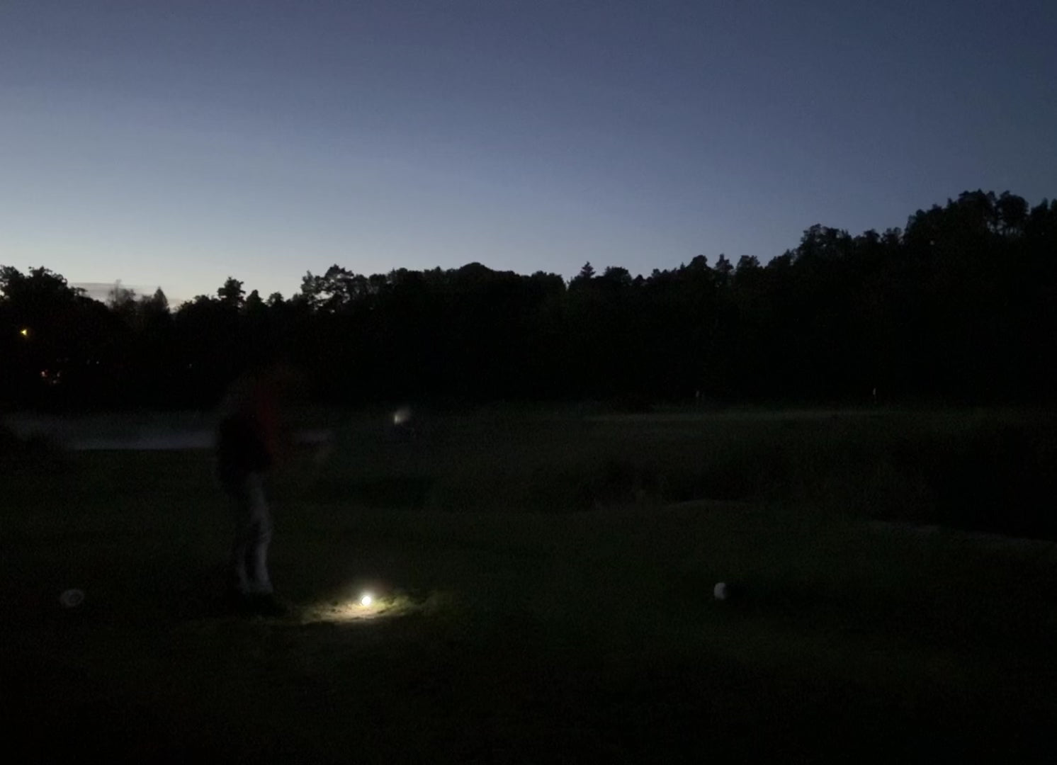 En person slår till en golfboll som börjar lysa upp på en golfbana